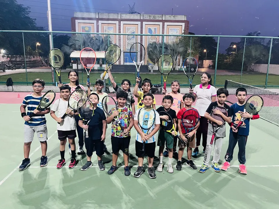 Junior group holding racquets on a floodlit court in the evening