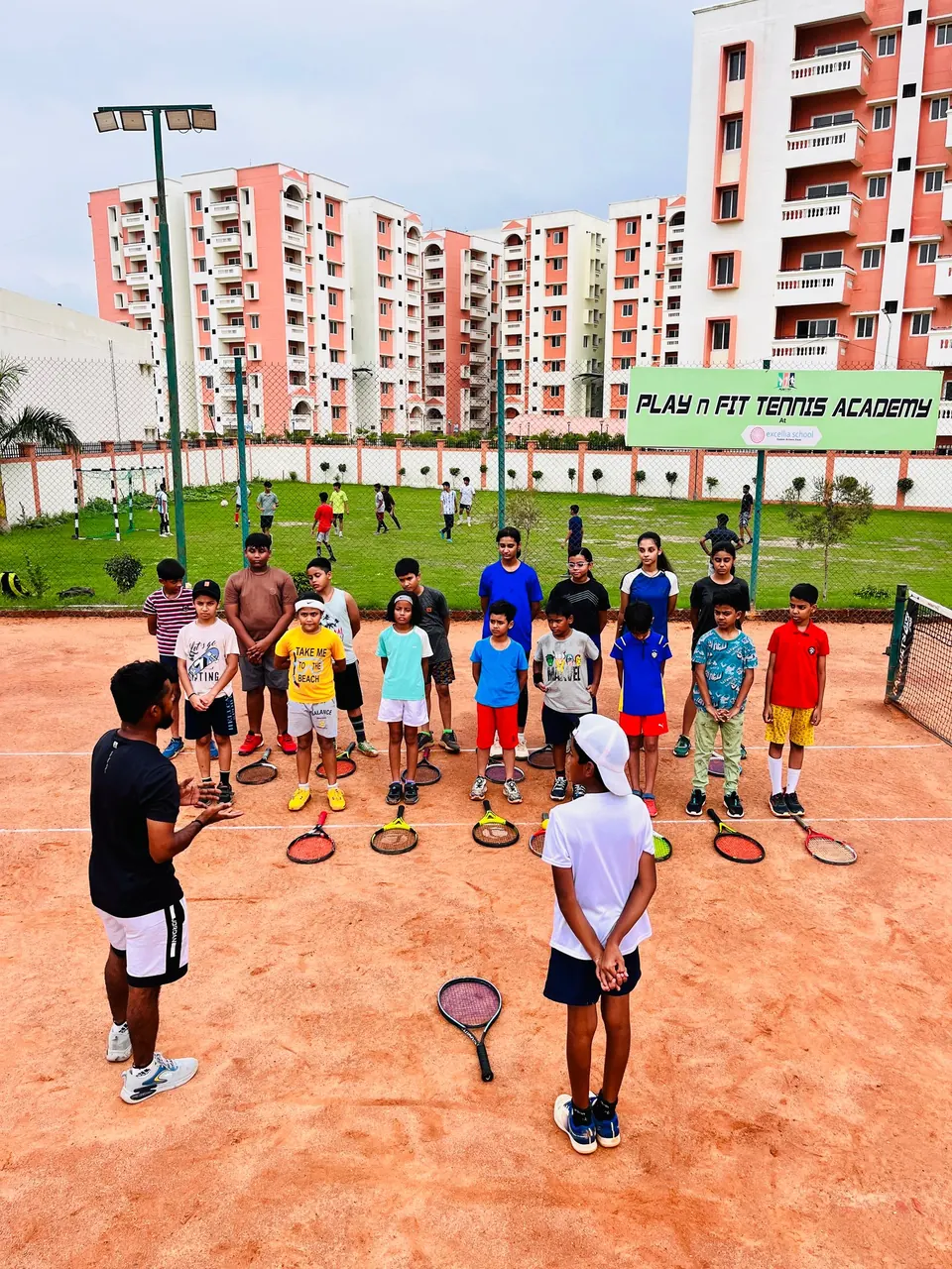 Coaches leading a large junior group with racquets on court