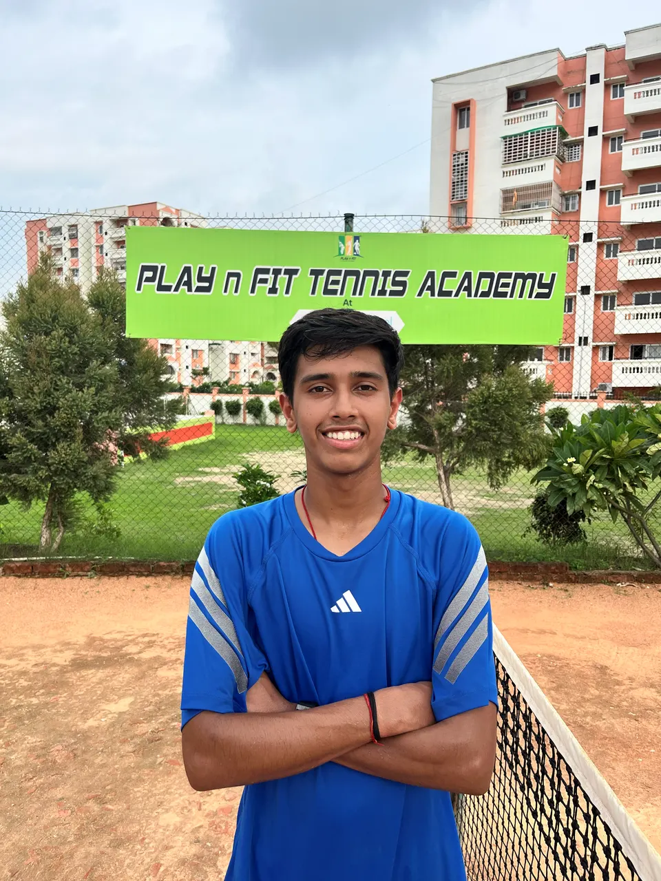 Kaustubh Singh at the PLAY n FIT Tennis Academy courts, arms folded beside the net
