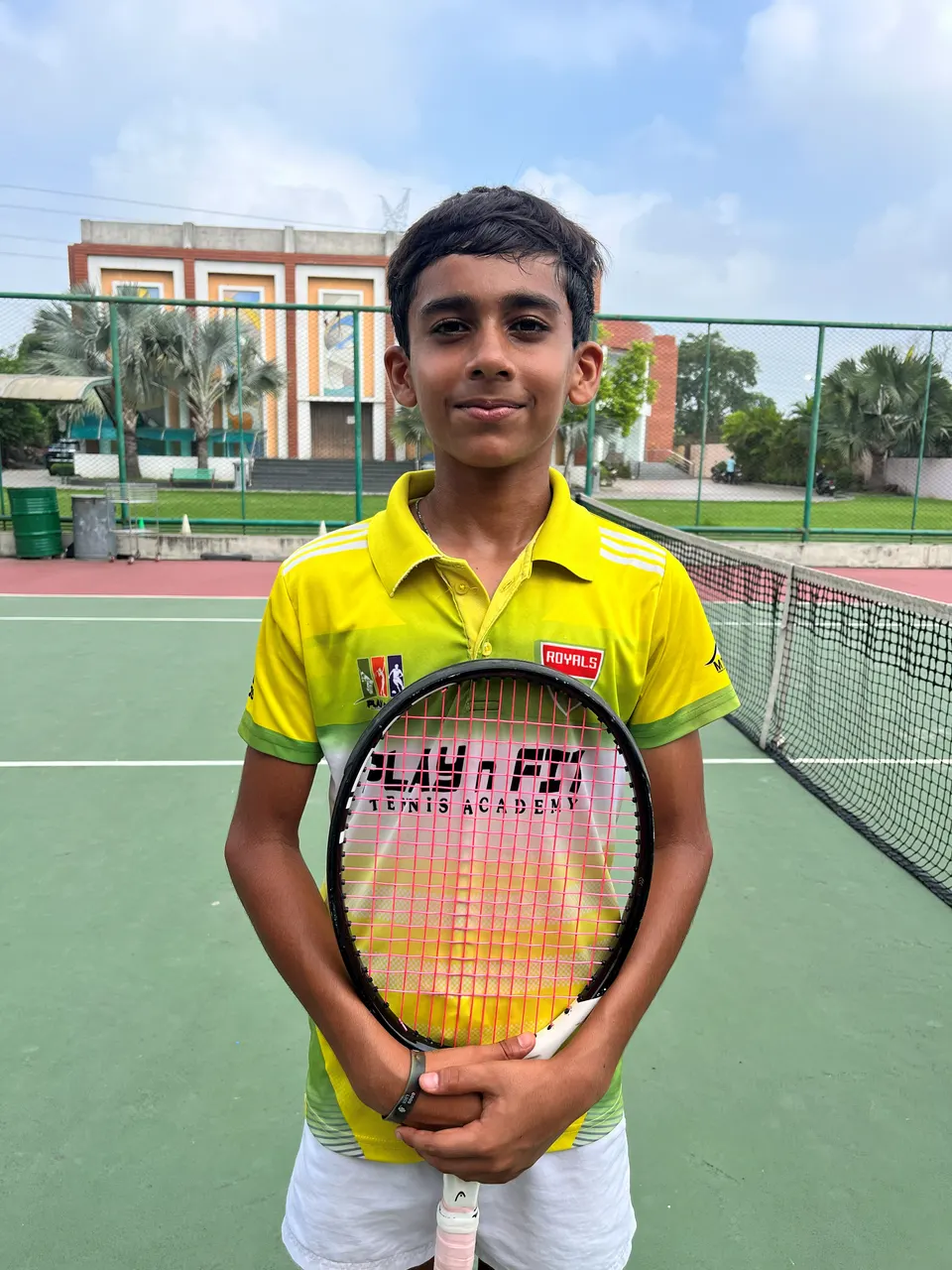 Tejas, a PLAY n FIT player, in the yellow academy kit holding his racquet on court